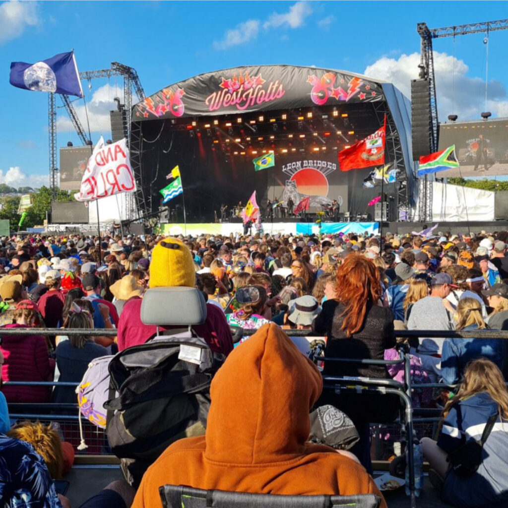 Three people sitting on a viewing platform in from of Glastonbury's West Holts stage