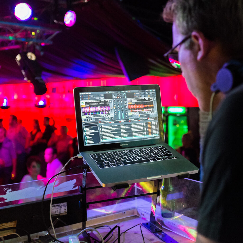 A man looking at a laptop screen at tha back of a room in a venue