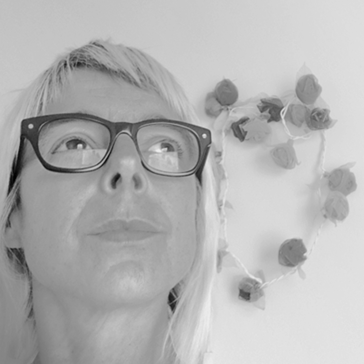 A white woman with blonde hair and chunky glasses stares upwards.