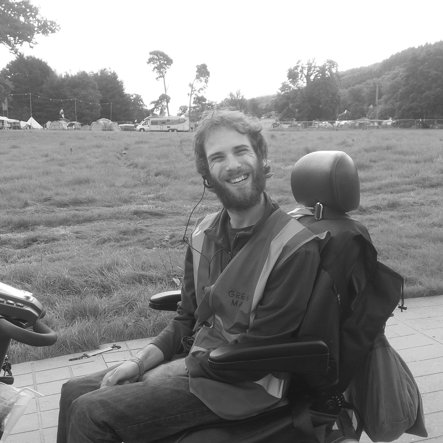 A white man with a beard sitting on a scooter in a field smiling.