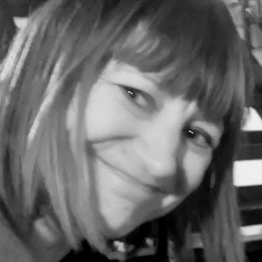 Headshot of Anna (Ania) Jezewska, smiling into camera, with shoulder length hair & full fringe