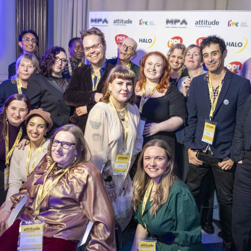 Attitude is Everything staff group photo at the end of a successful night. They’re standing in front of the step-and-repeat wall which shows logos for Attitude is Everything, and the event’s sponsors: Halo, PPL, LIVE, and the MPA.