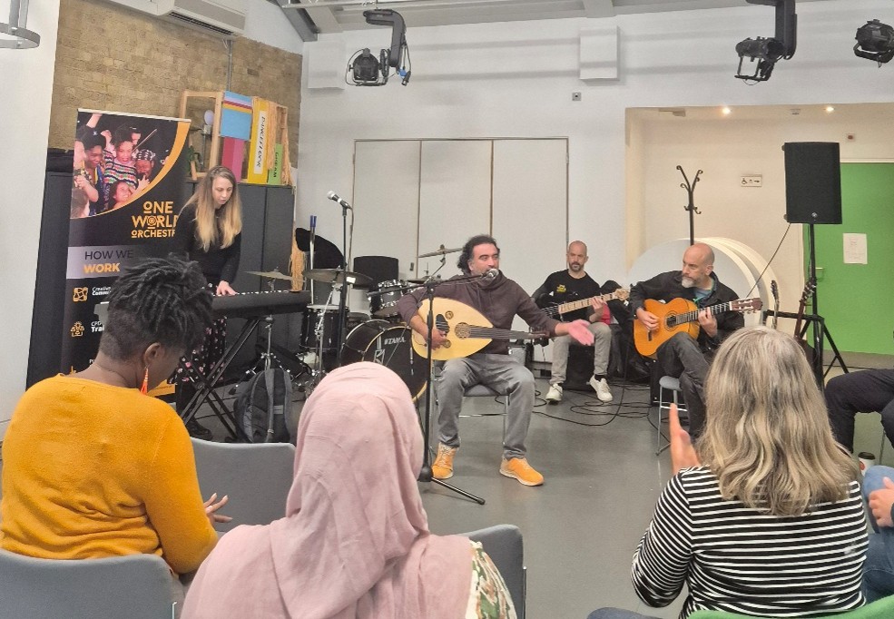 A group of musicians playing guitars and keyboard, in front of an audience with their backs facing the camera.